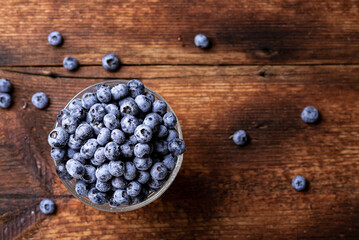 Wall Mural - Fresh tasty blueberries in a glass bowl on a dark wooden background.