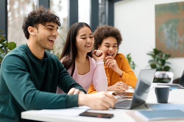 Happy three diverse friends studying together in coworking space, learning with laptop preparing for university exam