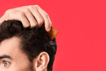 Poster - Young brunette man combing hair on red background, closeup