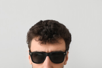 Poster - Young brunette man in sunglasses on light background, closeup