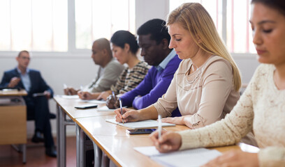 Wall Mural - Young woman sitting at desk in classroom working during lesson at adult education class