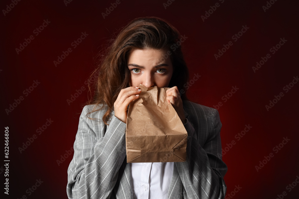 Young woman with paper bag having panic attack on dark background