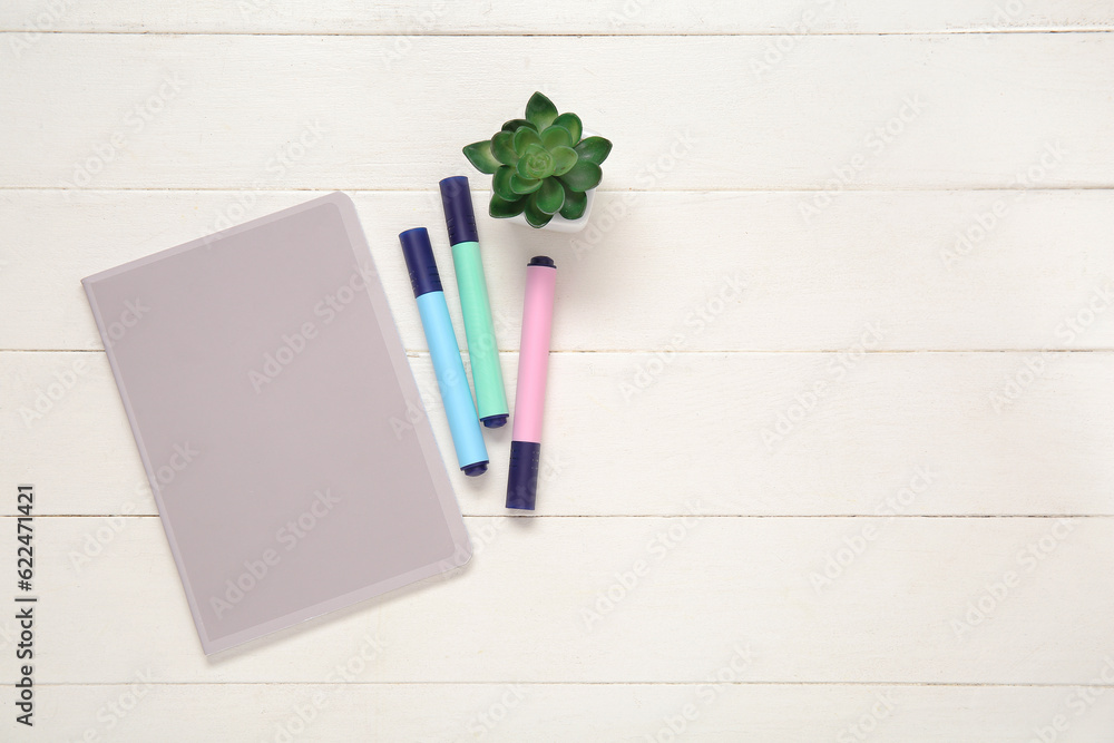 Notebook with markers and houseplant on white wooden background