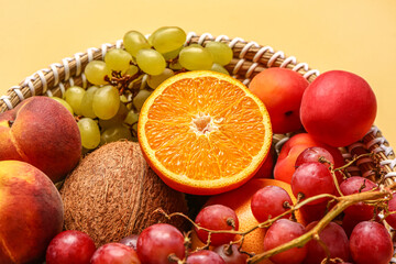 Wicker bowl with different fresh fruits on orange background, closeup