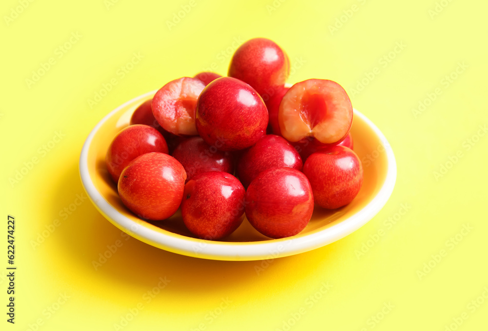 Plate with sweet cherries on yellow background