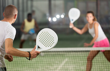 Wall Mural - Rear view of man with white racket playing padel tennis with friends at court