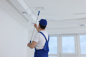 Poster - Handyman painting ceiling with roller in room, back view