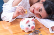 © nuwatphoto - Coins on hand are dropped in Piggy banks with cash piles on a wooden top table,