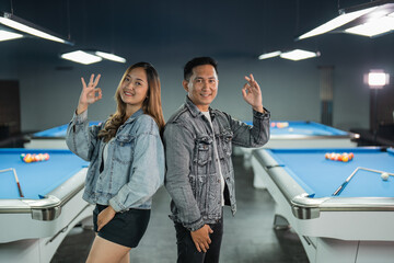 couple of billiard players standing back to back with oke hand gesture at the center of the billiard studio