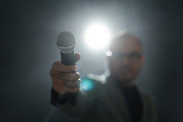 Confident successful speaker man talking on stage with spotlight strike through the darkness at corporate business event. Public speaker giving talk at conference hall. Stand up comedian.