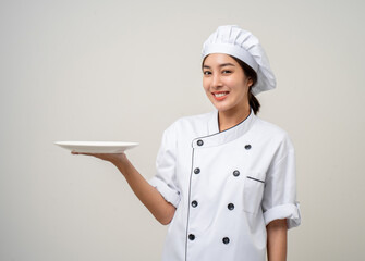 Wall Mural - Smiling Young beautiful asian woman chef in uniform holding empty plate delicious dish menu good taste on isolated. Cooking woman Occupation chef or baker People in kitchen restaurant and hotel.