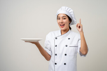 Wall Mural - Smiling Young beautiful asian woman chef in uniform holding empty plate delicious dish menu good taste on isolated. Cooking woman Occupation chef or baker People in kitchen restaurant and hotel.