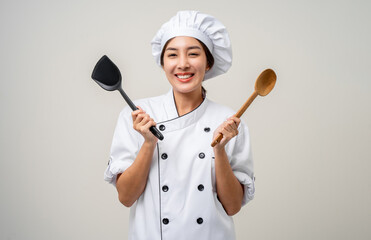 Wall Mural - Young beautiful asian woman chef in uniform holding ladle utensils cooking in the kitchen various gesture delicious dish menu good taste on isolated. Cooking woman chef people in kitchen restaurant