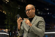 © Chanakon - Night scene. Senior manager business man in suit with cell phone at the buildings downtown. Confident man using smartphone looking towards their goals for success. Executive business man