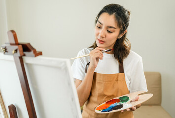 Wall Mural - Asian woman artist working on painting with brush and variant acrylic color. Female artist painter on canvas in creative studio as art concept