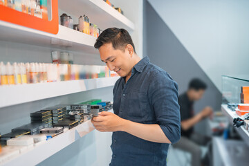 Wall Mural - male vape seller looking at his phone while standing beside the store shelf