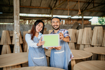 Wall Mural - Asian business couple smiles as they show a tablet screen at a woodcraft shop