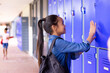 Happy biracial schoolgirl standing next to lockers in corridor at school