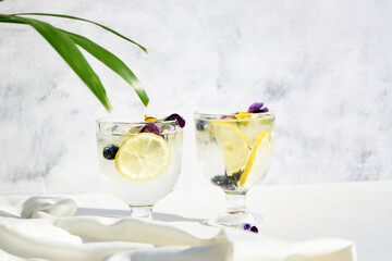 Wall Mural - Cold water with lemon garnished with edible flowers. Cool summer lemonade. Summer non-alcoholic cocktails and drinks.