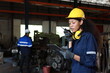© feeling lucky - Technician engineer or worker woman in protective suit using walkie talkie radio with tablet while controlling or maintenance operation work lathe metal machine at heavy industry manufacturing factory