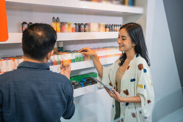 Wall Mural - female shopkeeper holding the digittal tablet while observing the liquids on the shelf together with the male shopkeeper