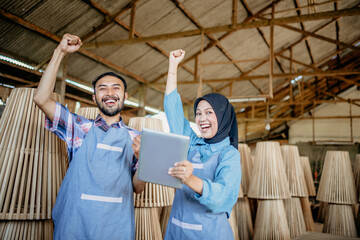 Wall Mural - excited entrepreneur couple raises their hands when using a tablet while working at the woodcraft shop