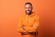 Portrait of a smiling man in orange hoodie standing with arms crossed isolated over orange background