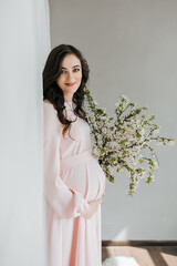 A beautiful pregnant woman in a pink dress holds her hands on her stomach. A loving mother is waiting for the birth of a child. Concept of pregnancy, motherhood, preparation and waiting.