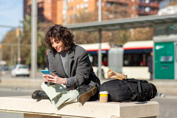woman using mobile phone while waiting at bus stop in city
