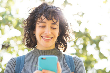 Wall Mural - Pretty young woman looking at cellphone standing outside on a sunny day