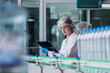 © eakgrungenerd - woman factory worker sterile uniform manufacture drink water. Female specialist factory line for processing and checking bottles water. Industrial product manufacturing aqua drink.