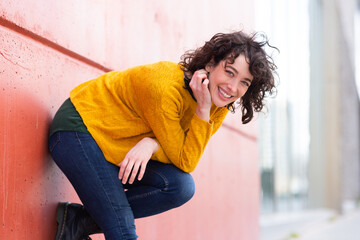 Wall Mural - Attractive woman bending over and smiling by a wall