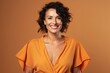 © igolaizola - Portrait of a smiling woman in orange dress isolated over brown background