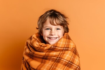 Wall Mural - Portrait of a little boy wrapped in a plaid on a orange background