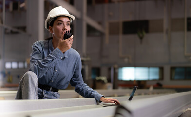 Wall Mural - Factory female worker using laptop computer checking, talking to supervisor in heavy metal production facility. Woman technician in white hardhat working, inspecting quality control in manufacturing.