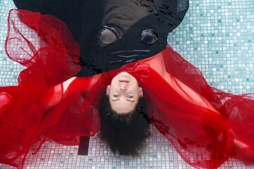 Top view of beautiful young sexy brunette nude woman relaxed covered by black and red cloth dress lying elegant in the water of the spa wellness pool