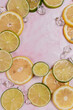 lemon and lime slices and ice in water on pink marble background