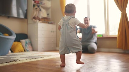 baby first steps. baby goes to her father at window learns to walk to take first steps. happy family