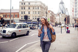 Fototapeta Londyn - Young woman using a phone while walking in the city london