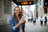 Fototapeta Londyn - Young woman using a smart phone while waiting at a bus stop