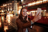 Fototapeta Londyn - Young woman taking a selfie at night while walking in the city london