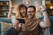 © Miljan Živković - couple man and woman husband wife play smart phone video games at home