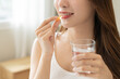 © KMPZZZ - Dietary supplement, asian young woman, girl hand holding medical pill capsule, take or eat vitamin C, D for treatment for skin, hair and nail strengthen with glass of pure water at home, healthcare.