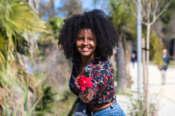 Young, beautiful black woman with afro hair holds a red flower in her hands. The beautiful woman is happy and smiling.