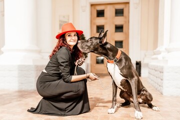 A photo of a woman and her Great Dane walking through a town, taking in the sights and sounds of the urban environment.