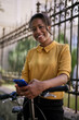 © kerkezz - Happy young woman with bicycle using mobile phone in city park, smiling.
