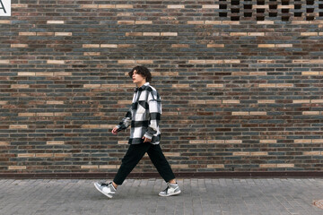 young man walks down the street in front of a brick wall