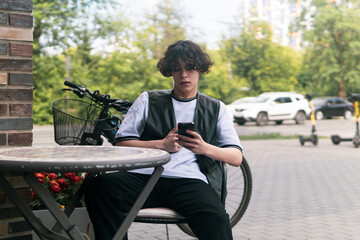 young man dialing something on the phone while sitting at an outdoor cafeteria table