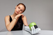 Young girl with disability wearing sensory bionic prosthetic arm seats at the table in studio. Beautiful woman holds a green apple in the artificial robotic hand. Full life after limb loss.