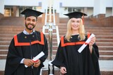 Fototapeta Londyn - education, graduation and people concept - happy international students in mortar boards and bachelor gowns.